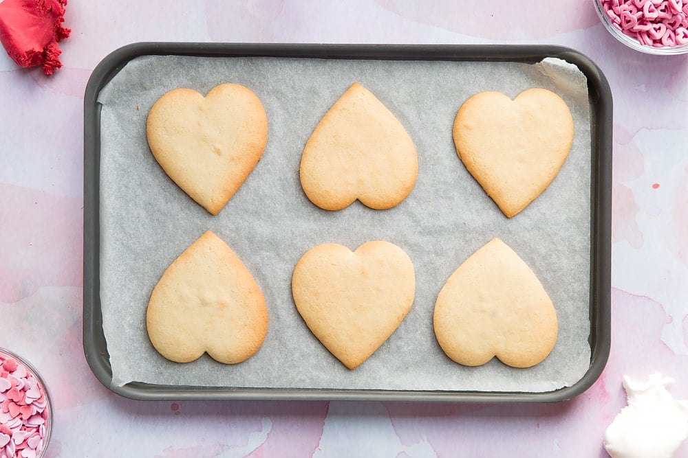 Overhead shot of baked heart shaped biscuits on a lined baking tray