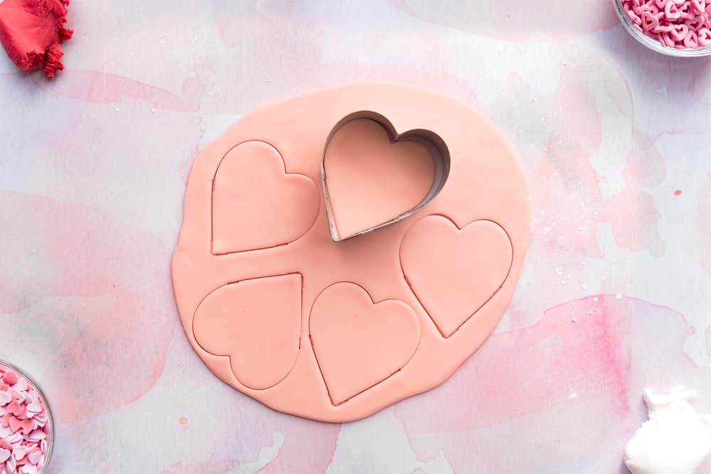 Overhead shot of a heart shaped cookie cutter cutting out pink heart shaped fondant