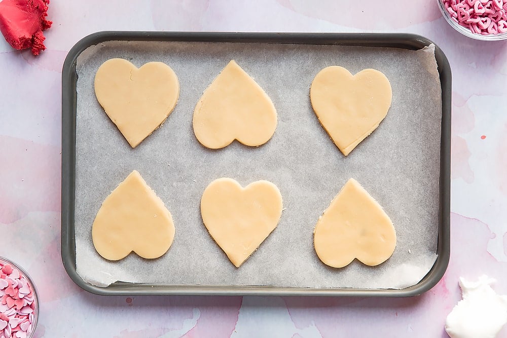 Overhead shot of heart shaped cookie dough biscuits placed on a lined baking tray