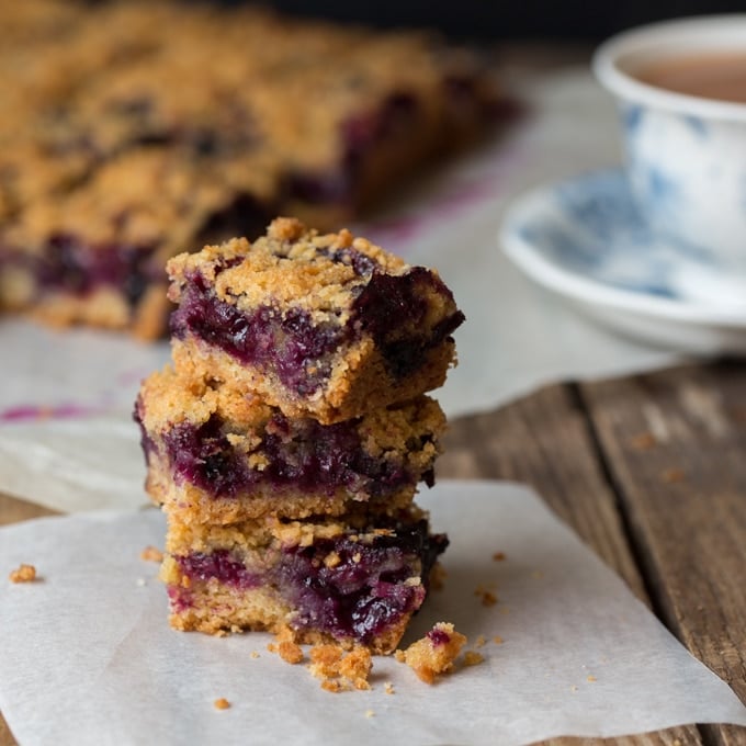 stacked Blueberry Crumble Slices on a greaseproof paper base and a teacup in the background.