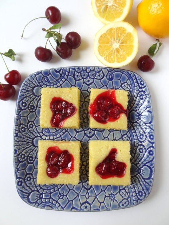 overhead view of Lemon cherry cake bars on a blue decorative plate with cherries at the side