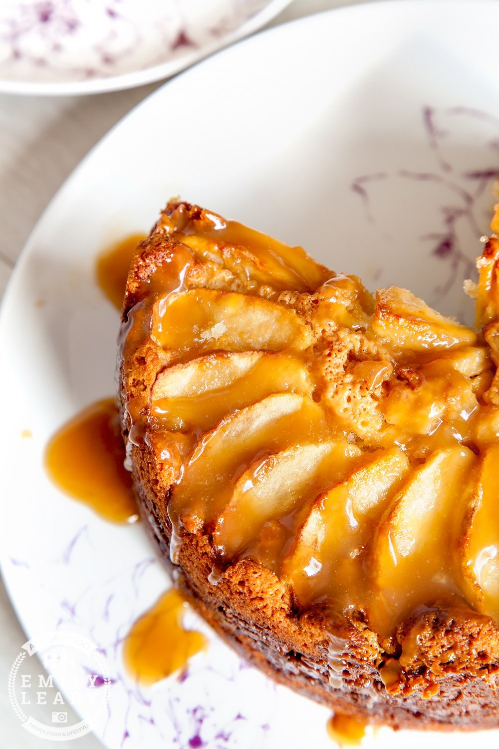 Toffee apple cake with a slice cut out placed on a white place with toffe sauce drizzled over the top.