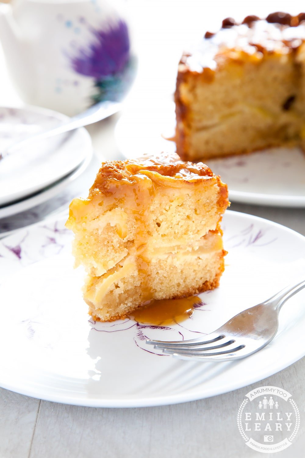 Toffee apple cake with a slice cut out placed on a white place with toffe sauce drizzled over the top.