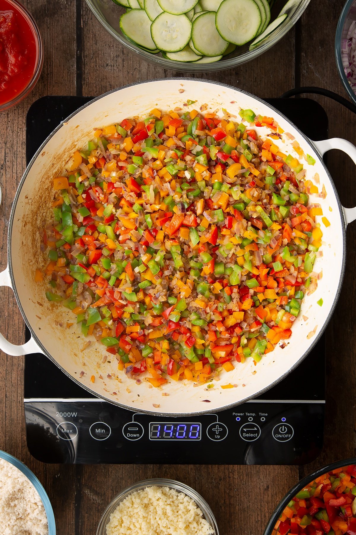 cooked onion and peppers mix in a large white frying pan on induction hob.