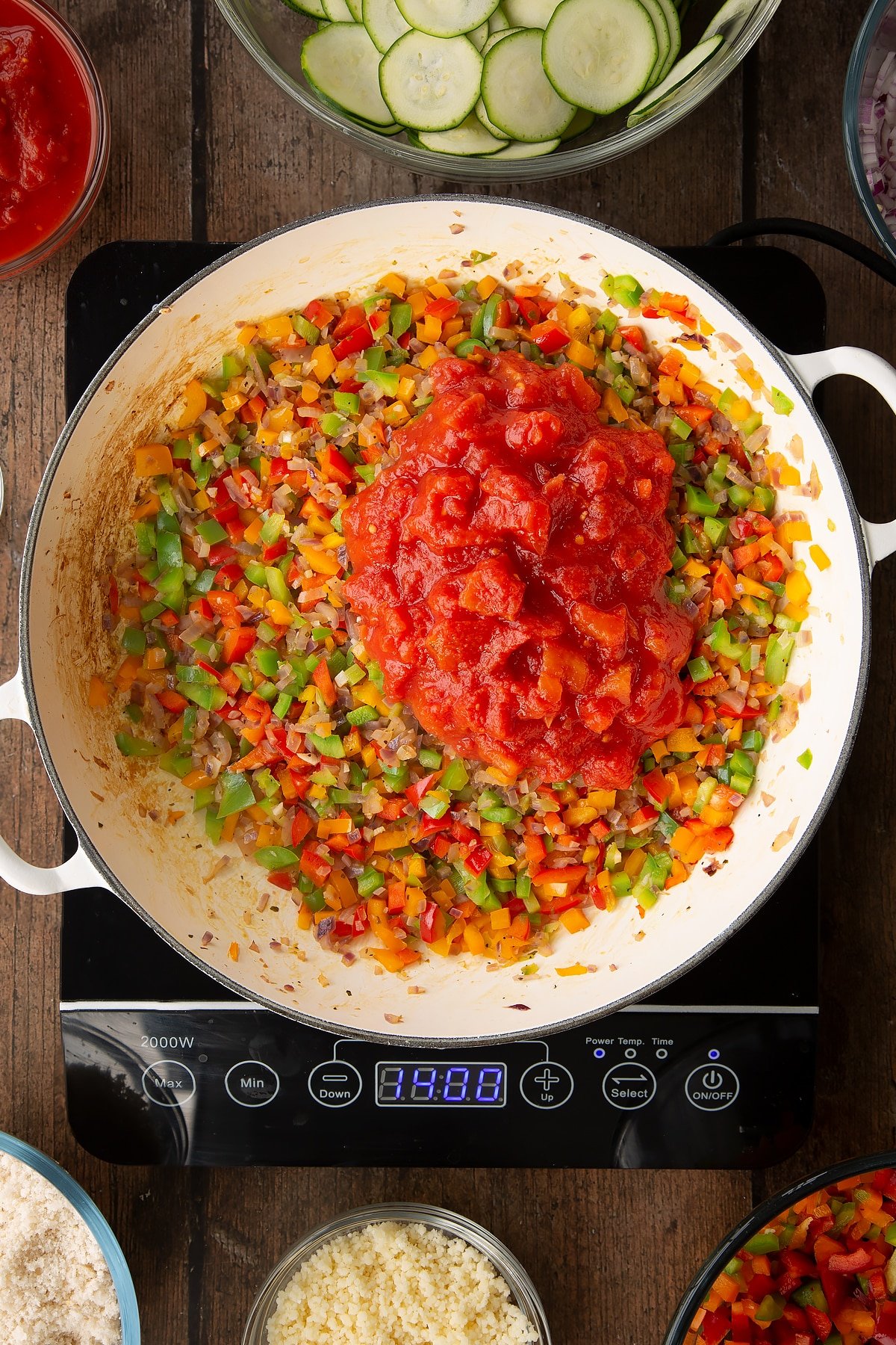 cooked onion and peppers mix topped with chopped tomatos in a large white frying pan on induction hob.