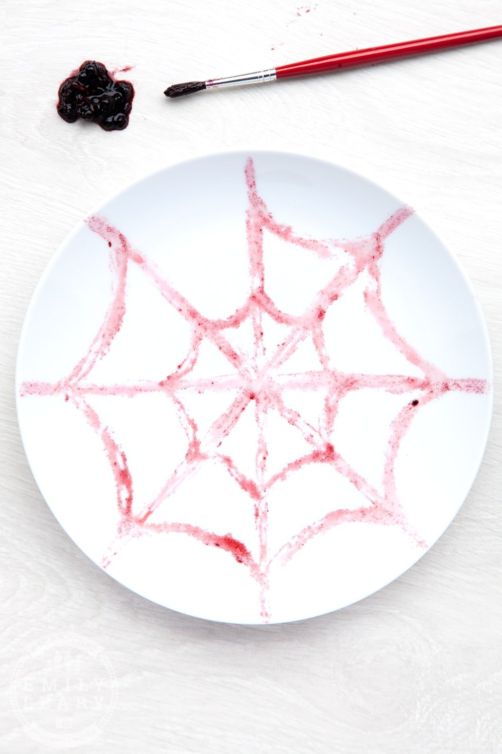 A white plate decorated with a spider web pattern using blackberry juice