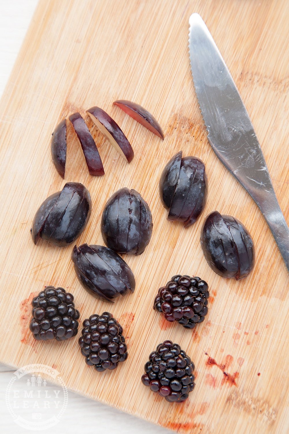 Sliced grapes and blackberries on a wooden board.