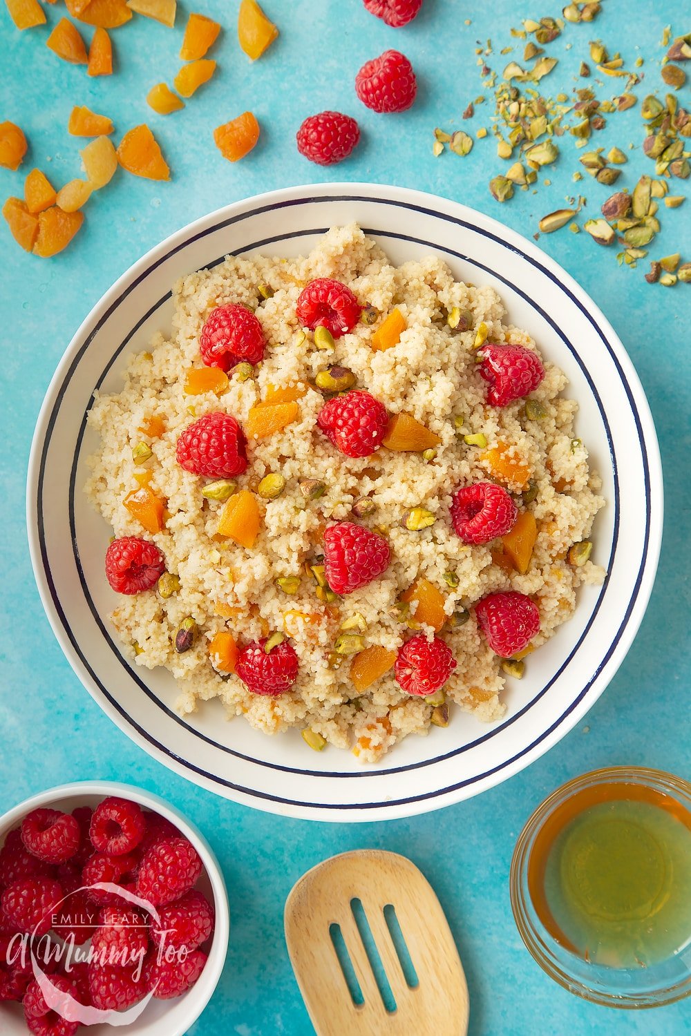 Overhead shot of a white bowl with black decoration filled with sweet breakfast couscous surrounded by ingredients for the recipe. 