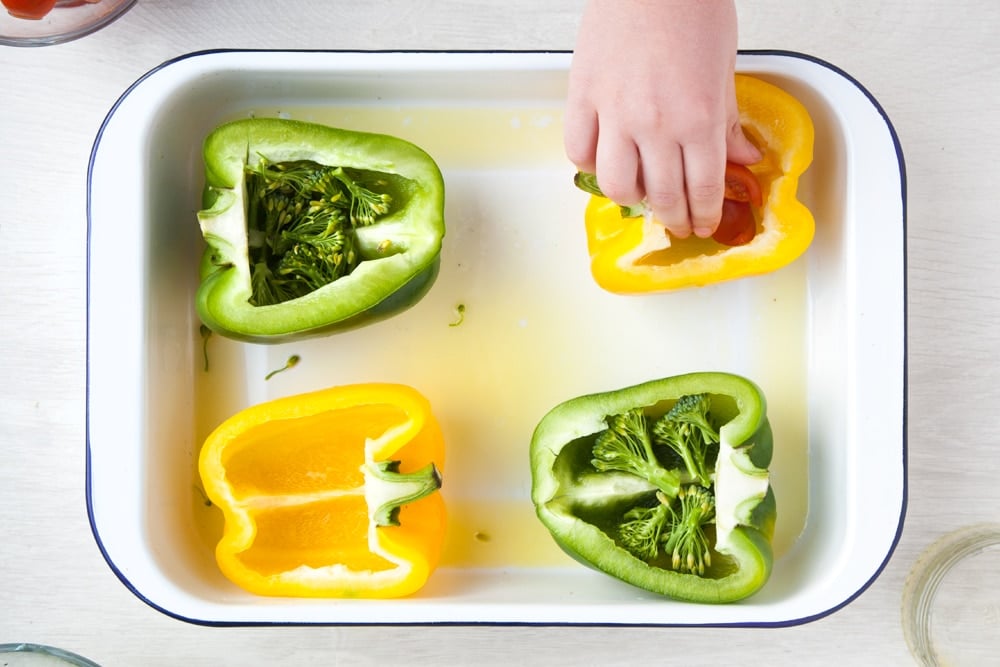 Adding cherry tomatoes to the pepper cups which already contain broccoli. 