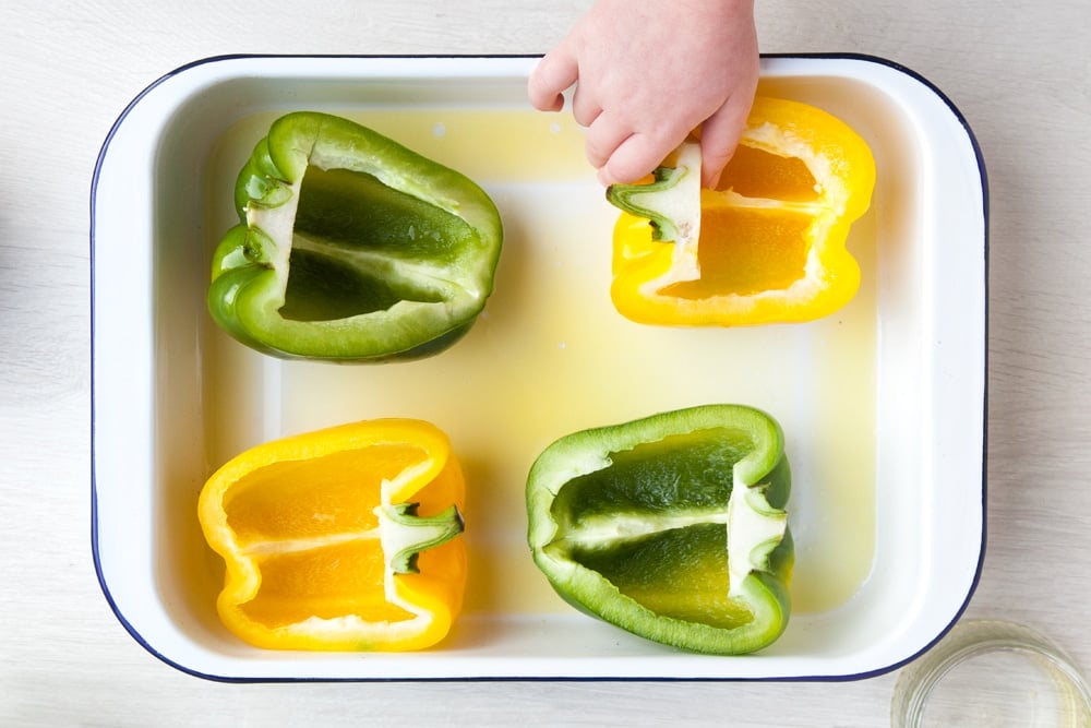One green pepper and one yellow pepper cut in half facing upwards on a baking pan. 
