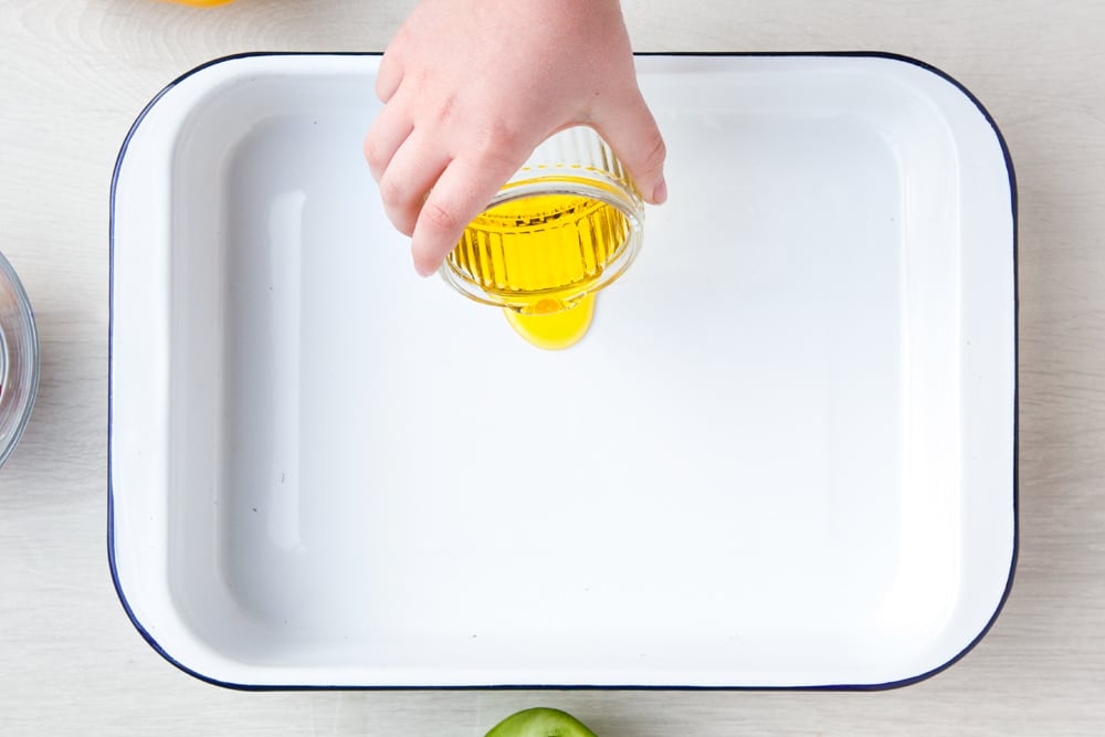 Prepare the baking tray with oil ready for the ingredients. The tray is situated on a white wooden background. 
