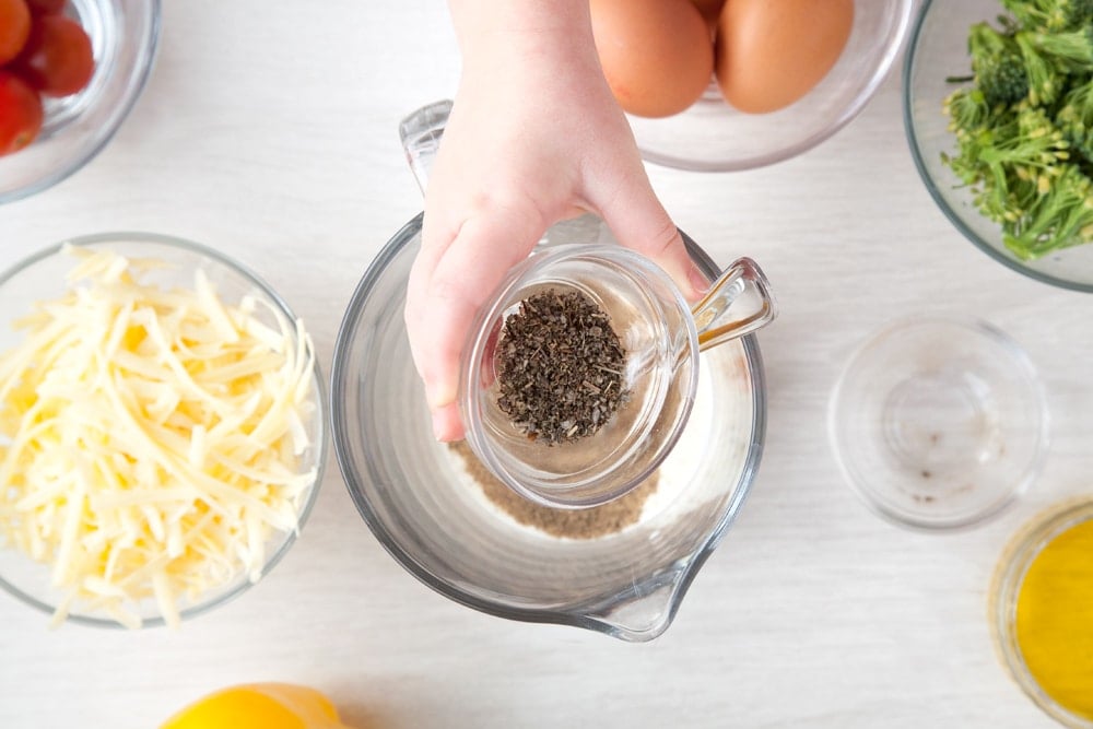 Mixing ingredients for the quiche filling in a jug on a white wooden surface.