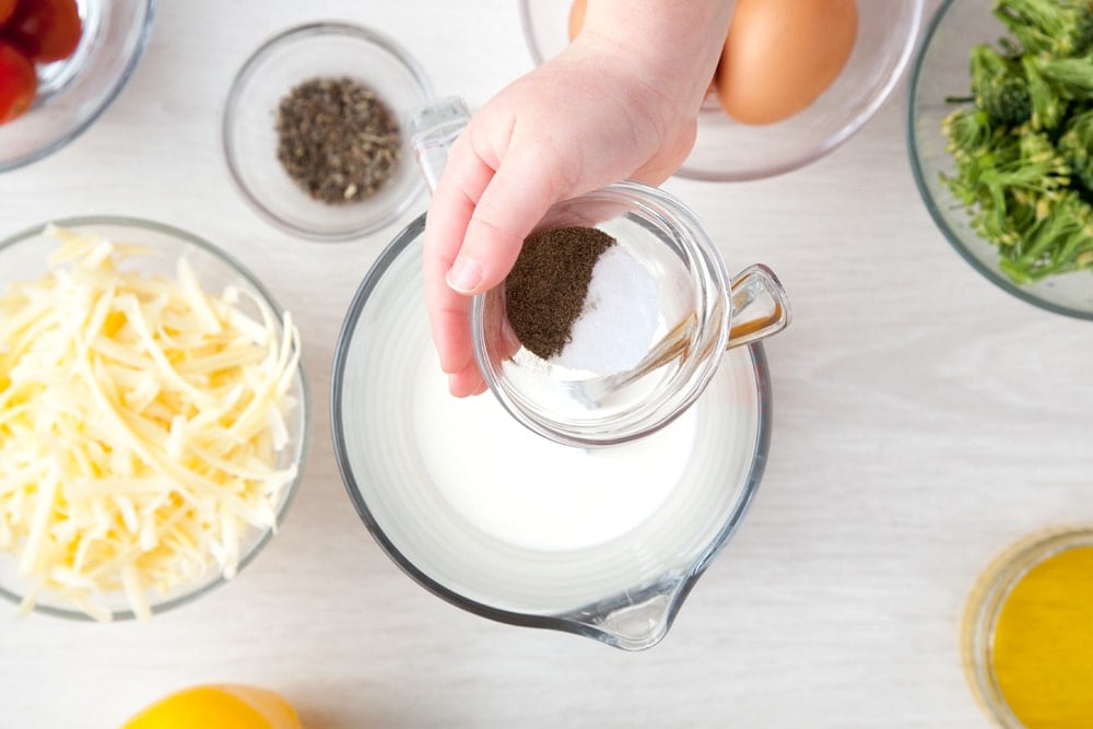 Making the quiche filling in a jug. Additional ingredients for the recipe are on the table in bowls.