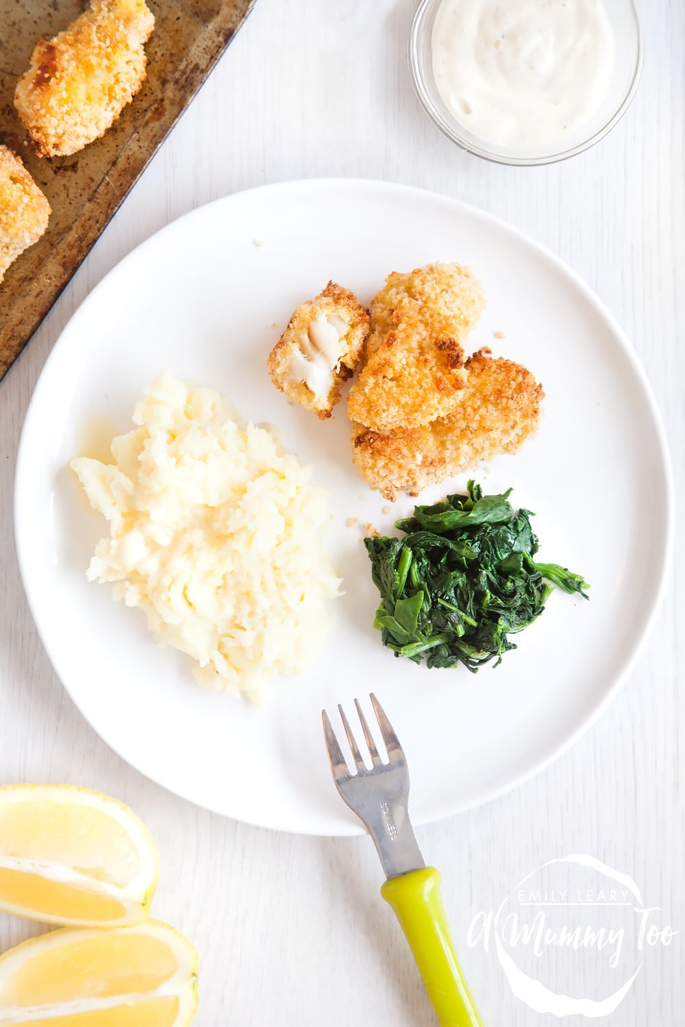 fish goujons one half eaten on a white plate with spinach and mash next to a dish of tartare sauce.