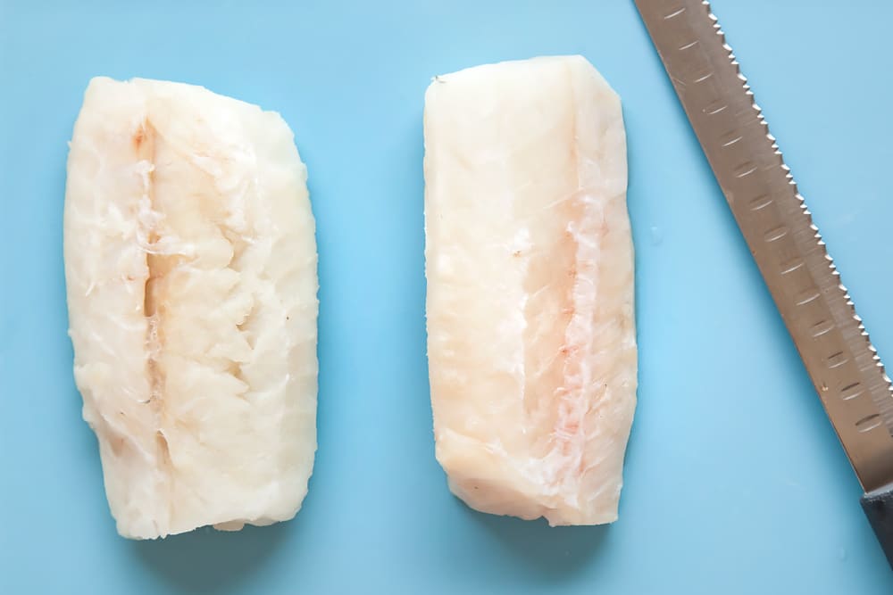 2 cod fillets with a sharp knife on a blue background.