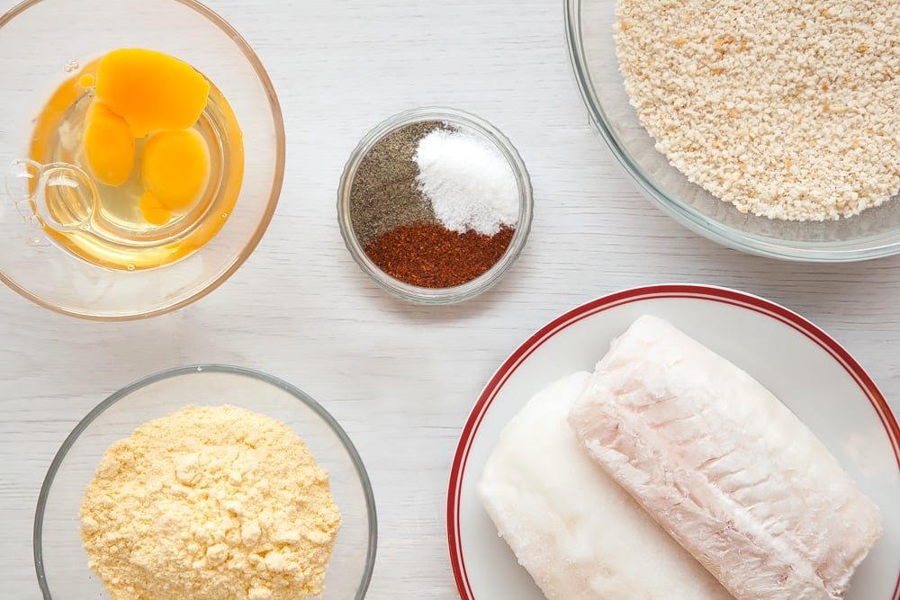 5 clear bowls holding ingredients to make fish goujons including spices, eggs, crumbs and fish.