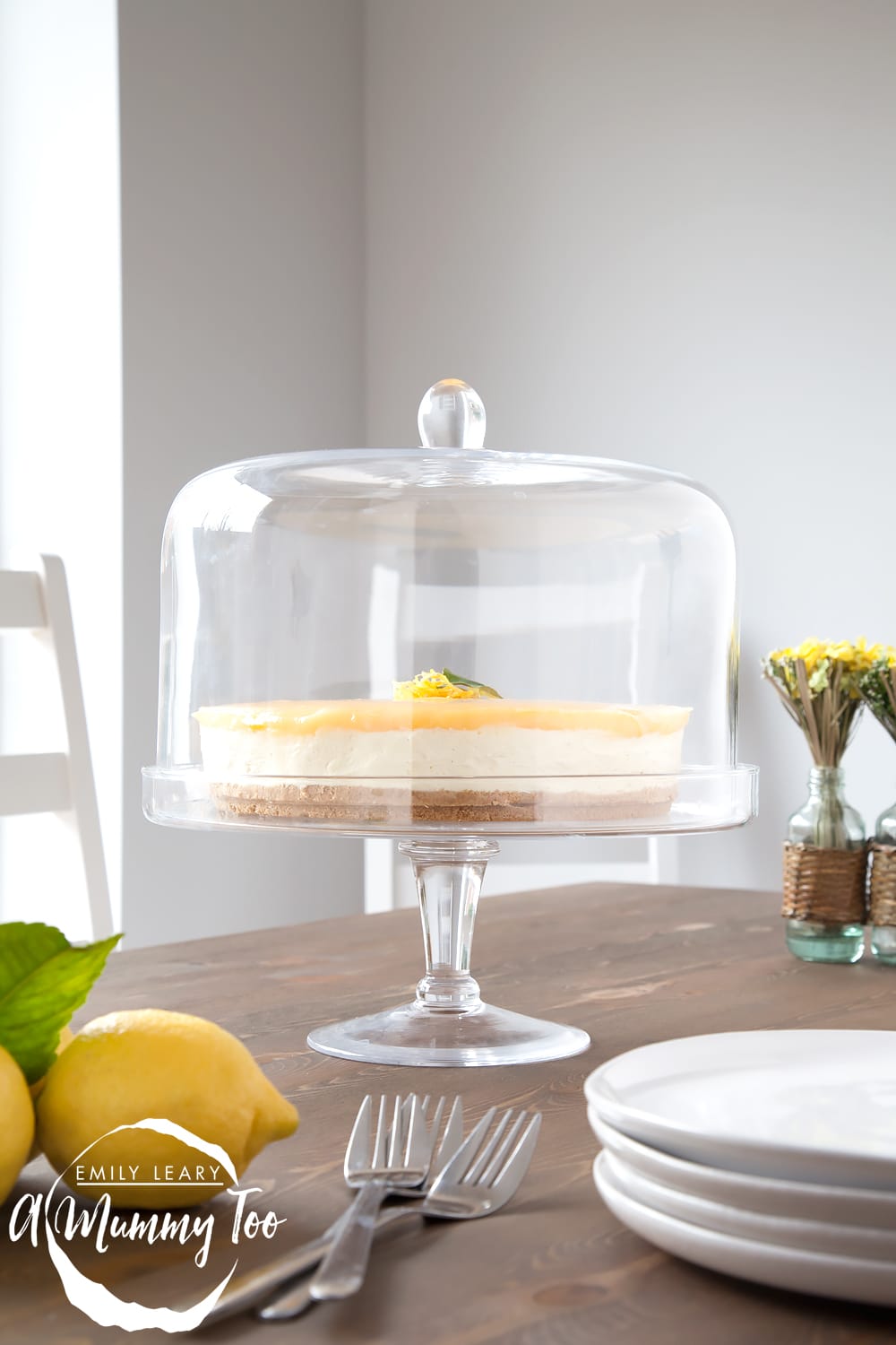 No-bake lemon curd and white chocolate cheesecake in a glass stand on a wooden table.