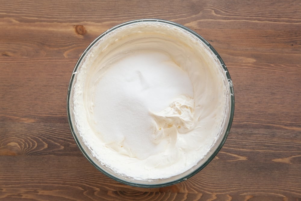 A bowl containing cream cheese, double cream and vanilla beaten together, topped with sugar. 
