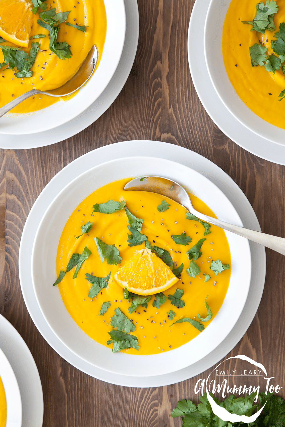 Orange, red lentil and roast carrot soup served in white bowls, garnished with parsley, orange slices and black pepper.