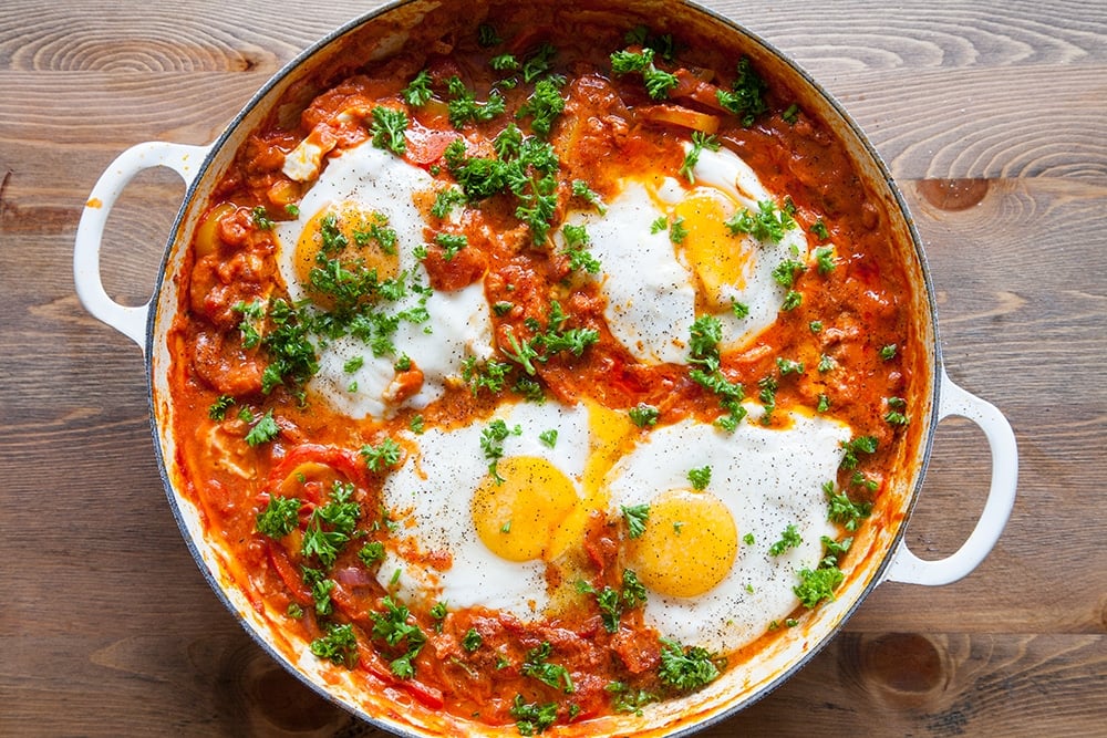 Overhead shot of spicy tomato sauce, cooked eggs and chopped parsley sprinkled on top in a casserole dish