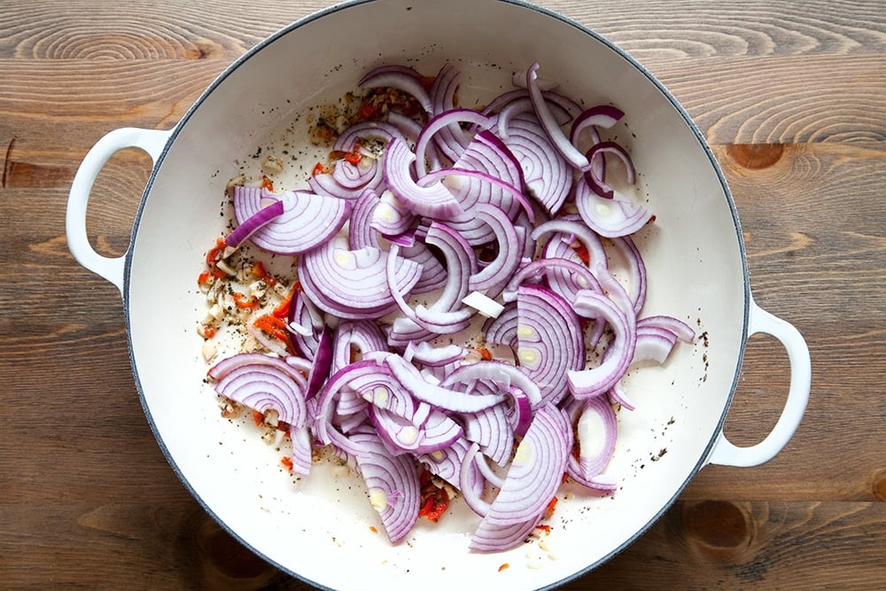 Overhead shot of Onion added to the spicy tomato sauce ingredients in a casserole dish