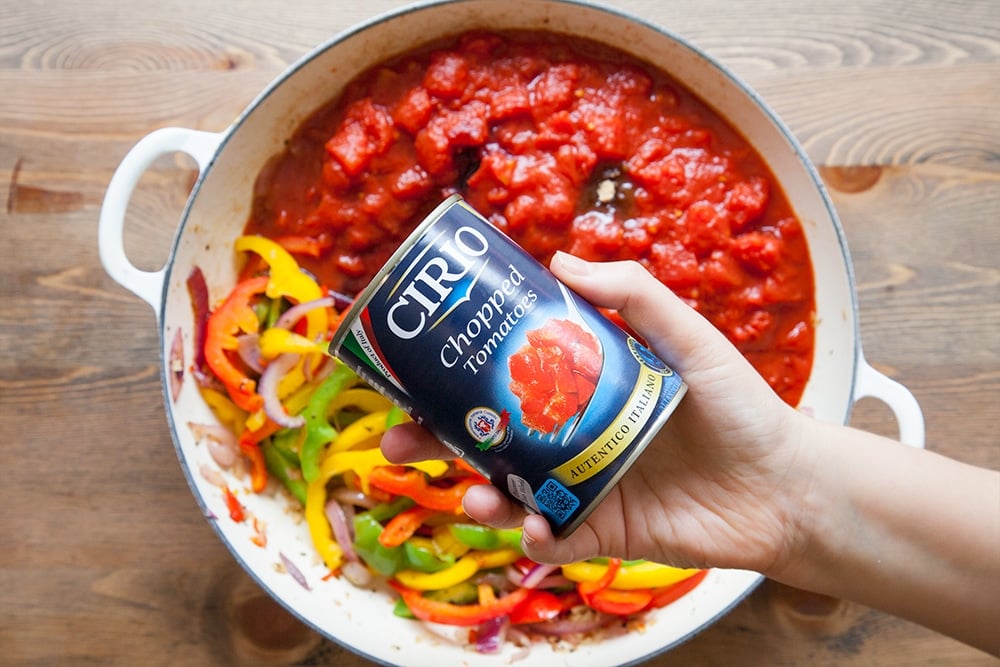 Overhead shot of a hand holding Cirio chopped tomatoes feature in this breakfast eggs in spicy tomato sauce recipe