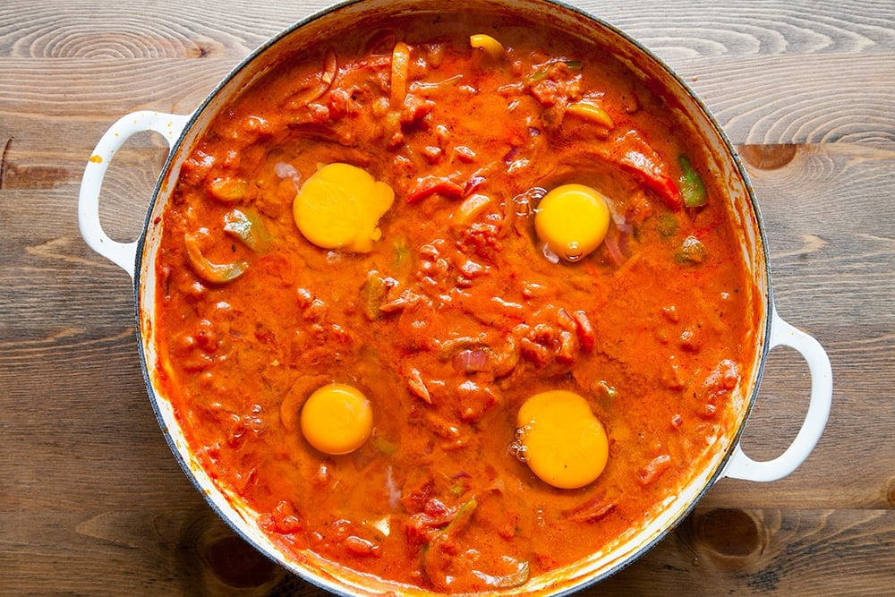 Overhead shot of spicy tomato sauce with 4 uncooked eggs on top in a casserole dish