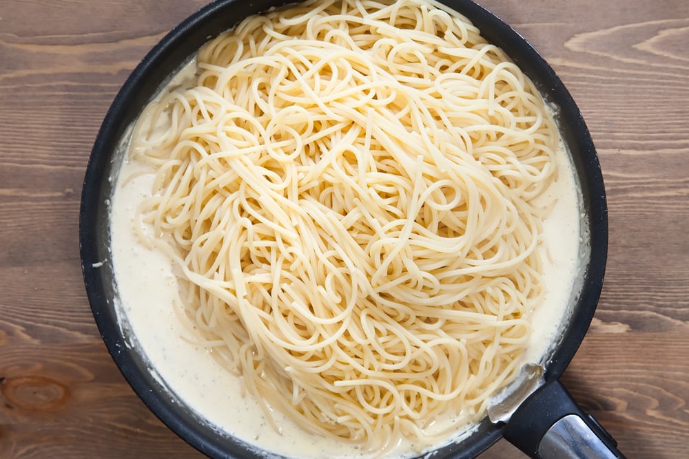 freshly cooked spaghetti topping a white cream sauce i a frying pan