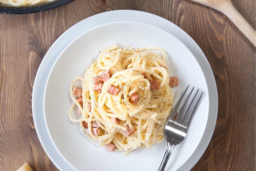 meat free spaghetti carbonara on a white plate with a fork on the side.