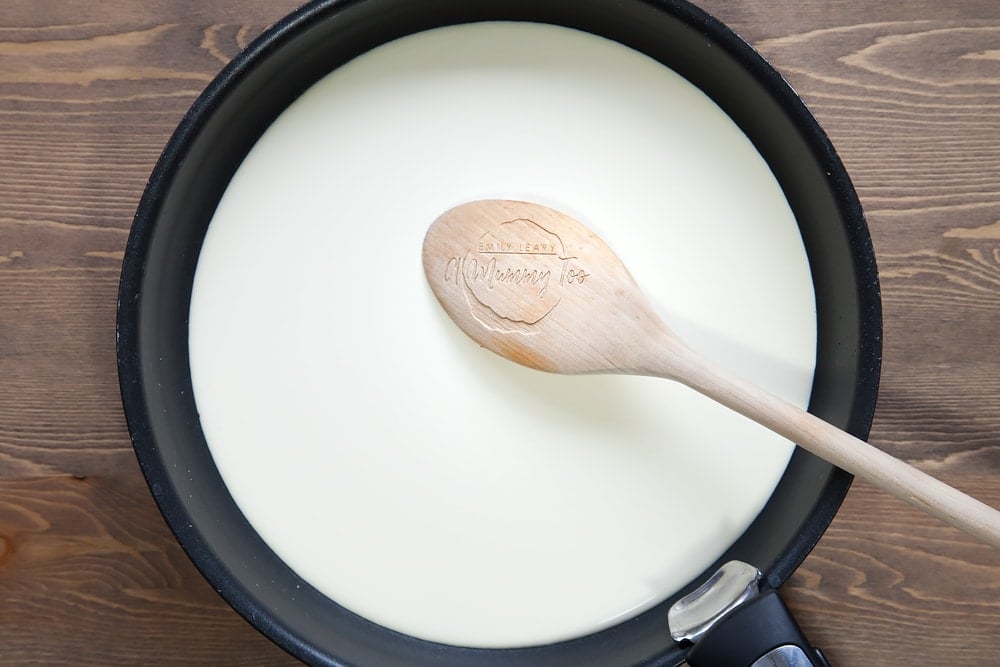 large frying pan with cream filled half way with a wooden spoon mixing.