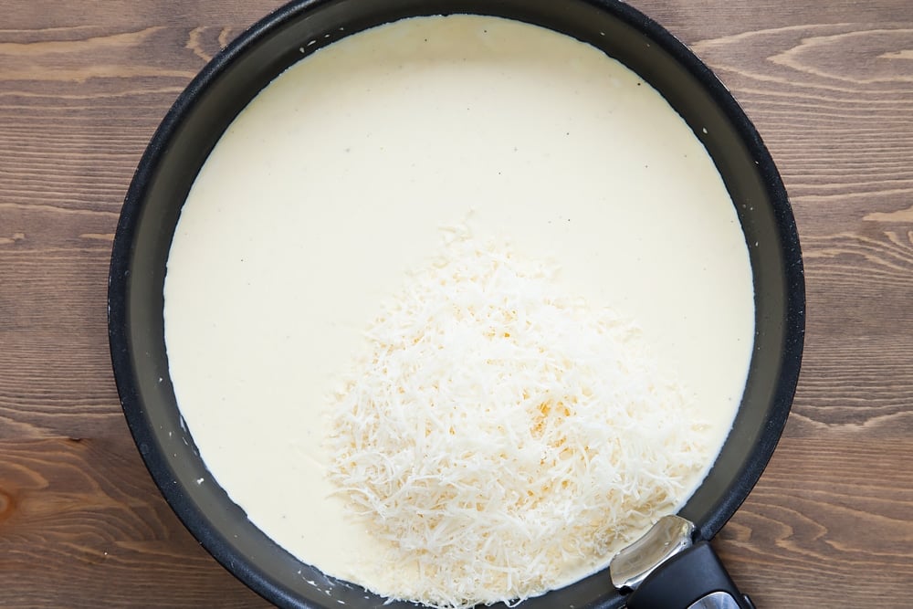 white creamy sauce in a frying pan topped with grated cheese
