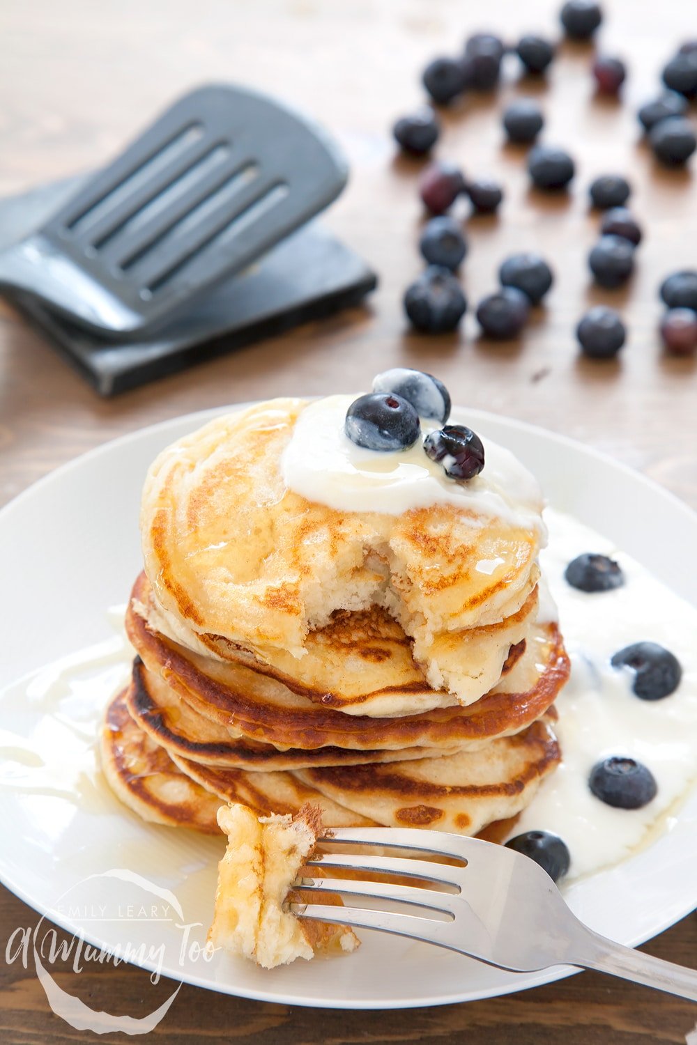 fluffy coconut yogurt pancakes, topped with blueberries on a white plate with a fork on the side.