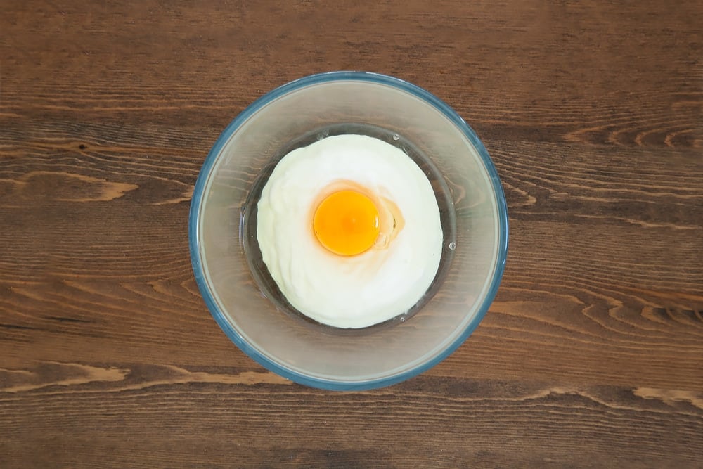 egg and yogurt in a clear bowl on a wooden background.