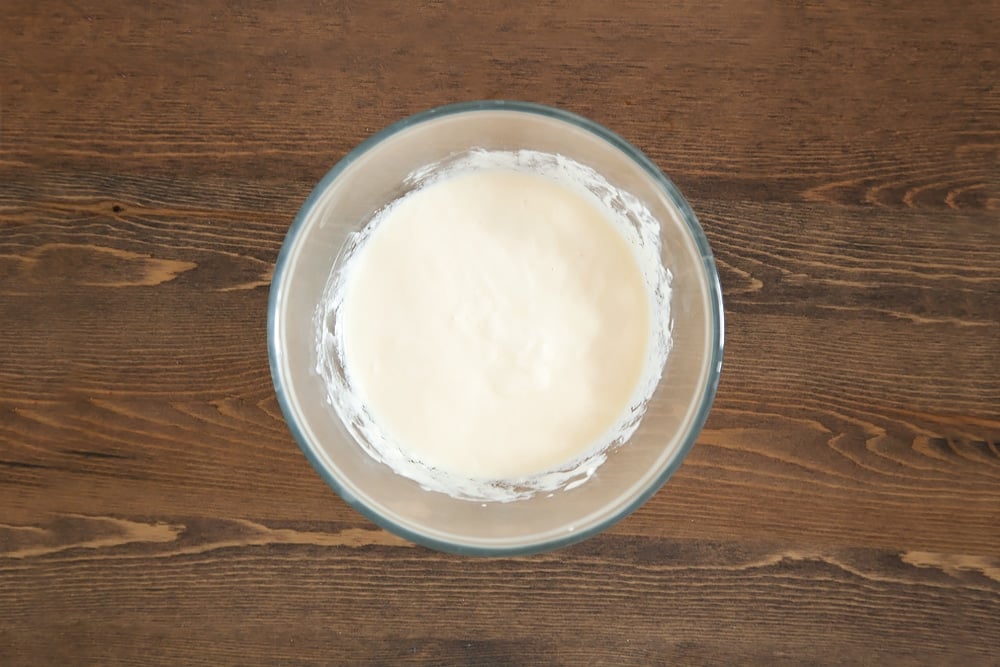 whisked egg and yogurt in a clear bowl on a wooden background.