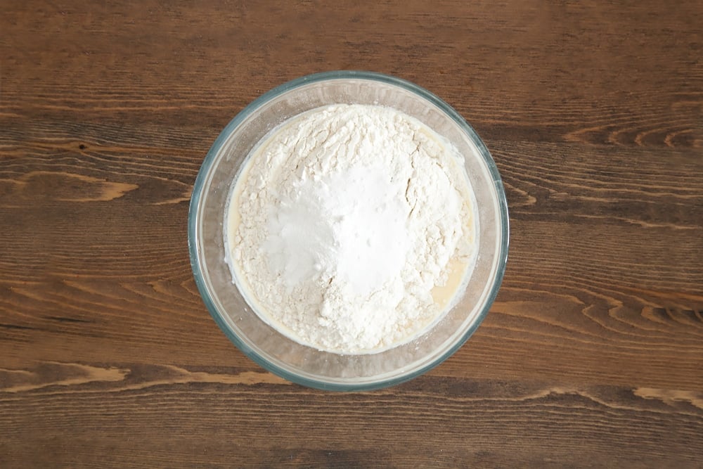 Whisked egg, milk and yogurt topped with flour and baking powder in clear bowl.