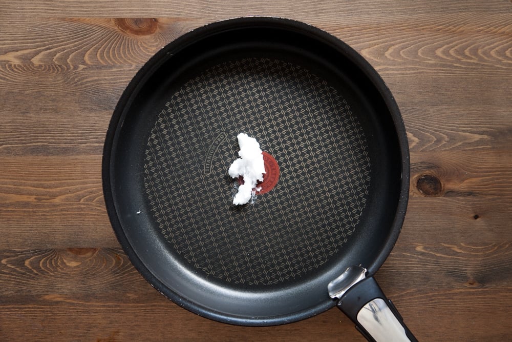 Coconut oil in a frying pan on a wooden background