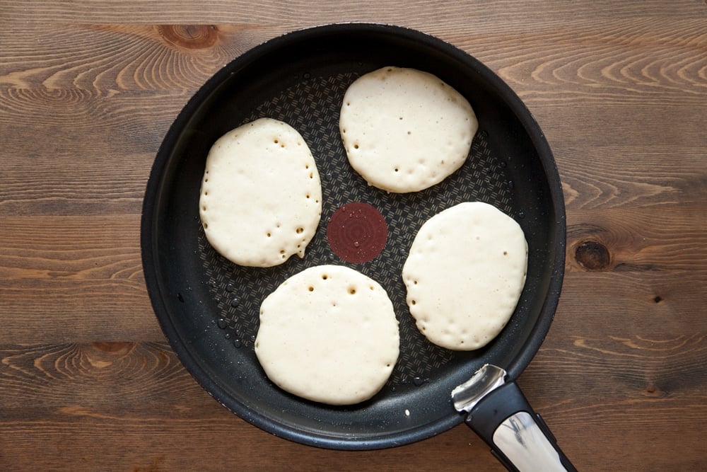 a large frying pan with 4 average size half cooked pancakes evenly spaced.