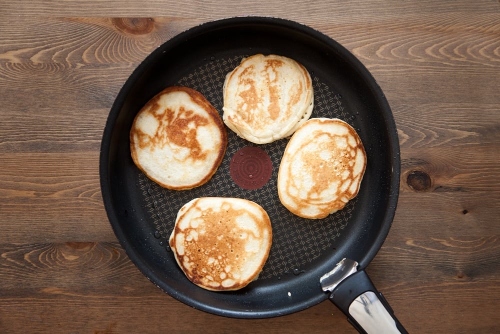 a large frying pan with 4 average size half cooked pancakes evenly spaced.