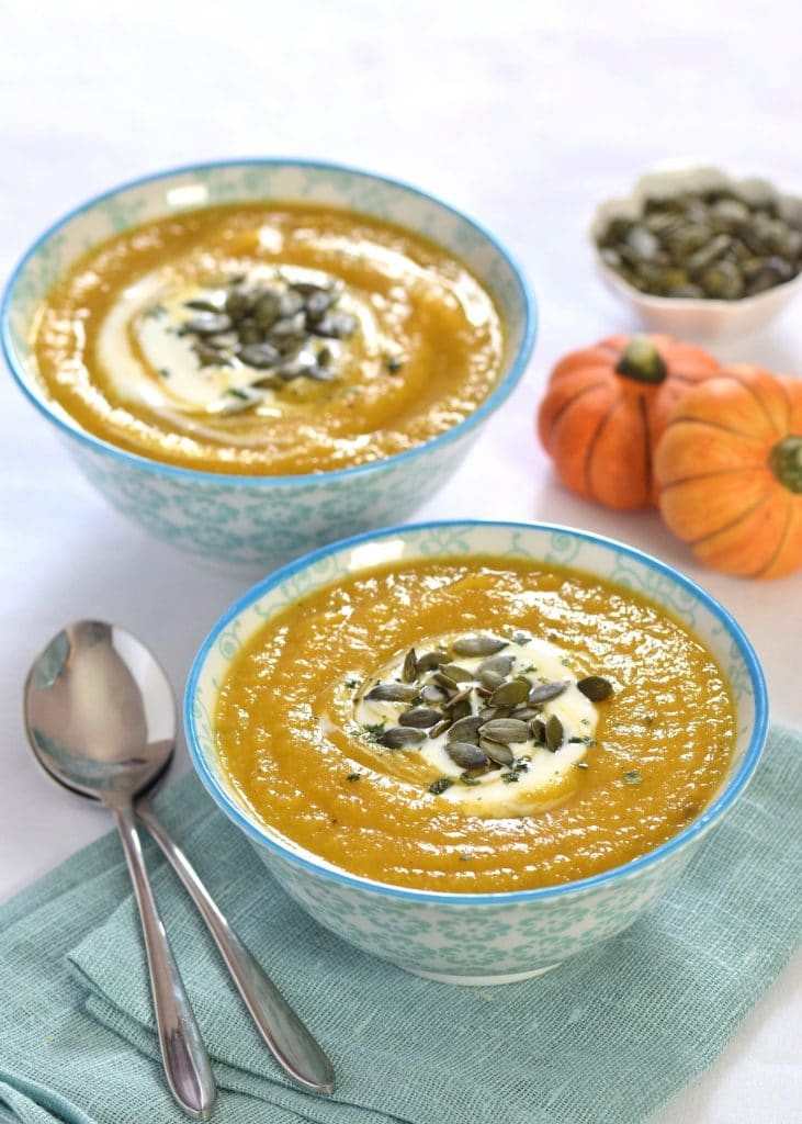 Curried pumpkin and parsnip soup served to two bowls, garnished with creme fraiche and pumpkin seeds.