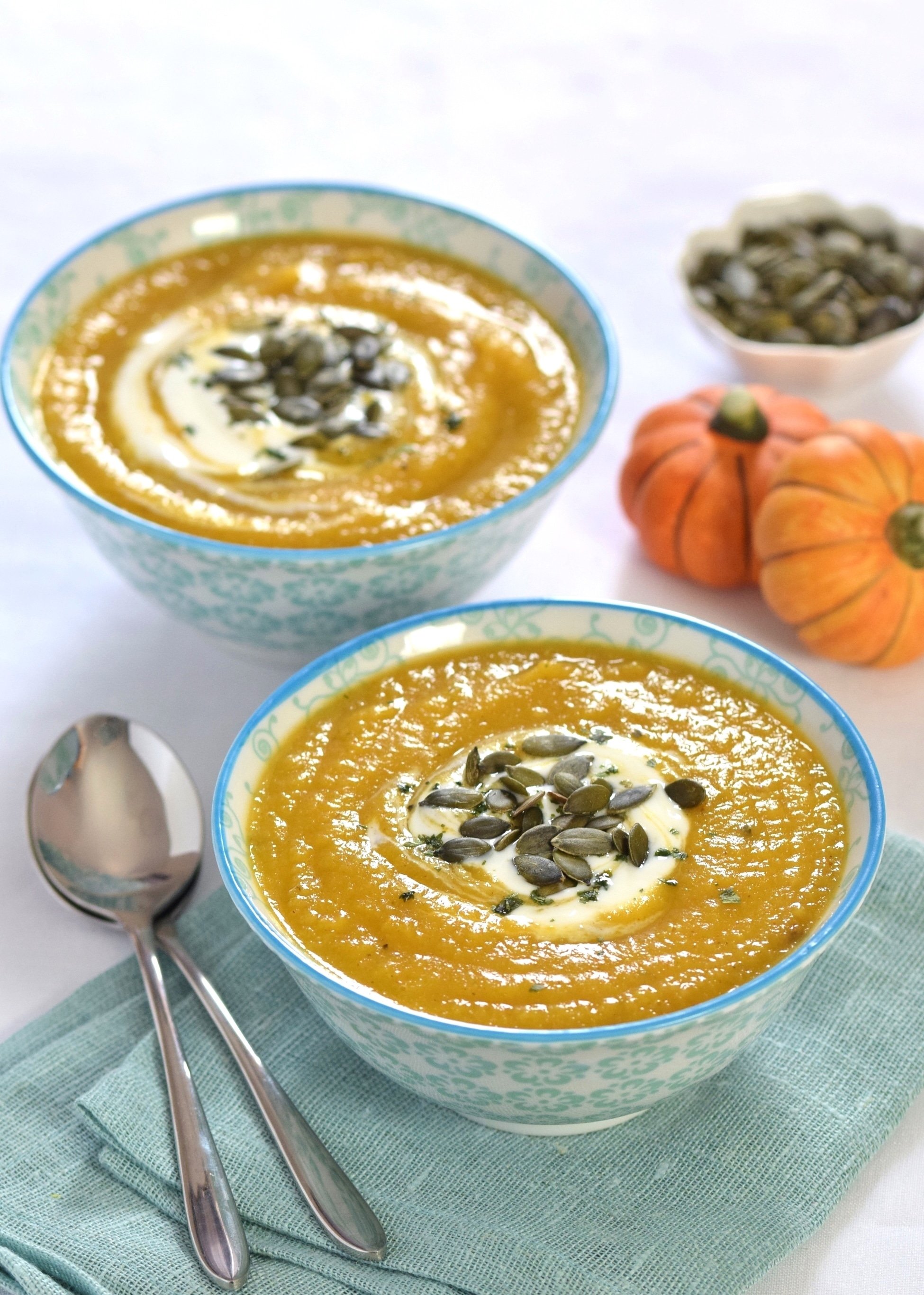 Curried pumpkin & parsnip soup served in blue and white bowls, garnished with natural yogurt, sprinkle of pumpkin seeds.