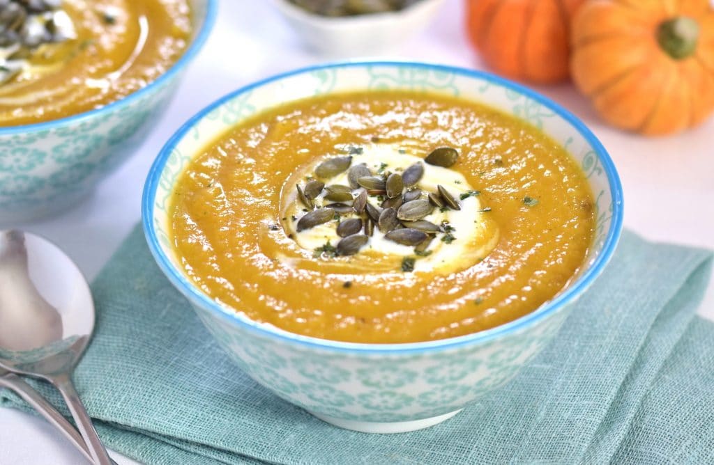curried pumpkin & parsnip soup in a colourful blue print bowl on a blue folded napkin topped with pumpkin seeds