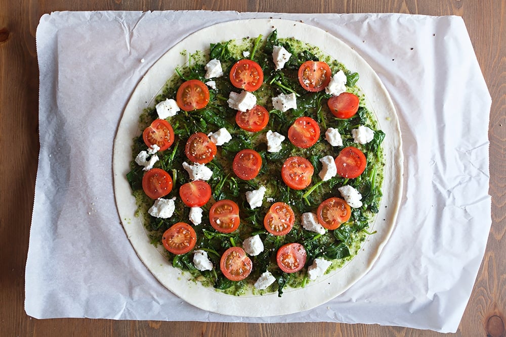 Assembling the gluten-free spinach and goat's cheese pesto tart - top the pesto with spinach, cherry tomatoes and crumbled goat's cheese