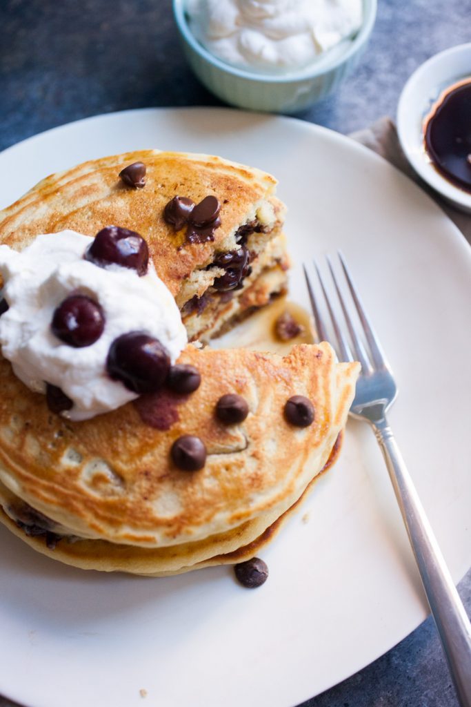 Cherry Chocolate Pancakes by macheesmo stacked on a white plate topped with yogurt and cherries