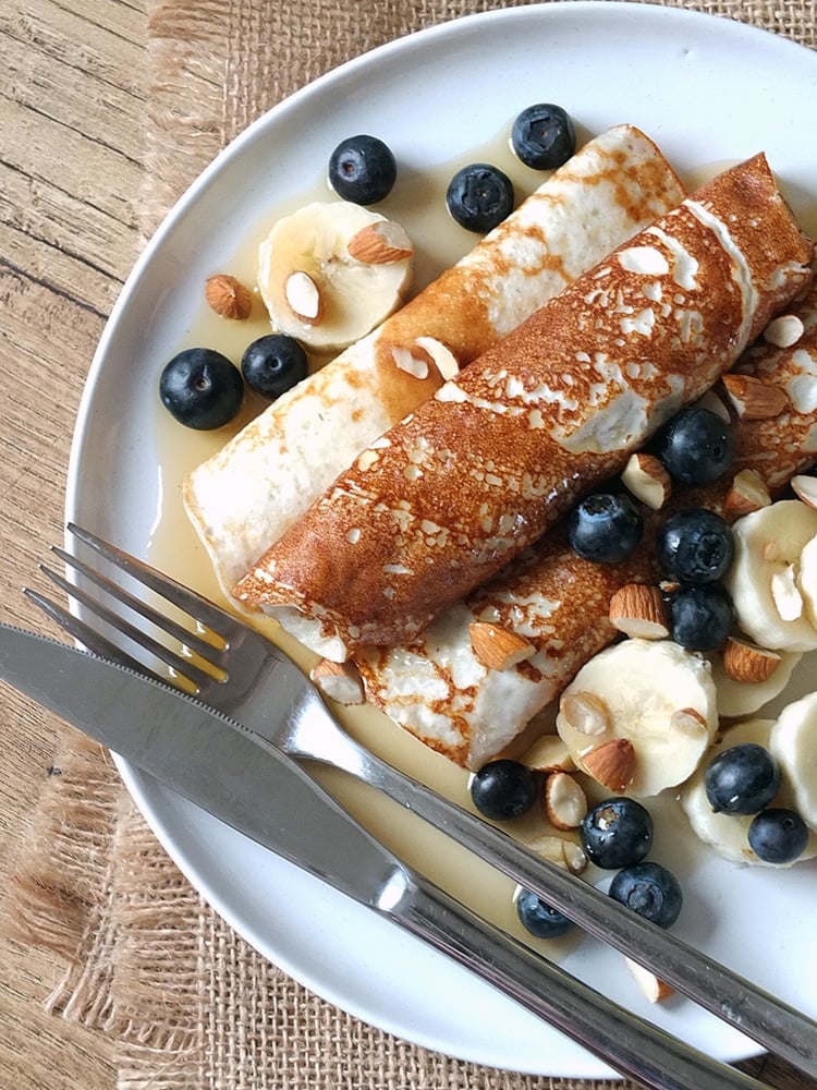 Cottage Cheese Pancakes by elizabeth's kitchen diary rolled up on a white plate topped with fruit, nuts and syrup.