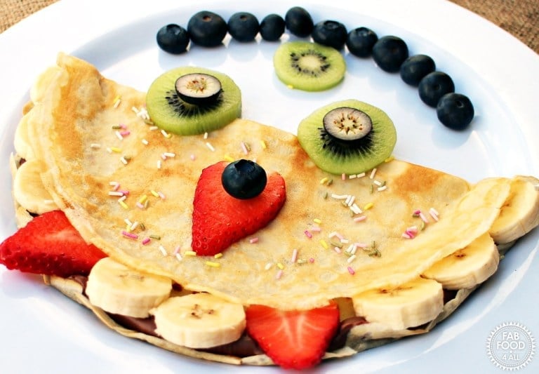 Monster Pancakes by fab food for all laid out on a white plate to create a face using fresh fruit and chocolate sauce.