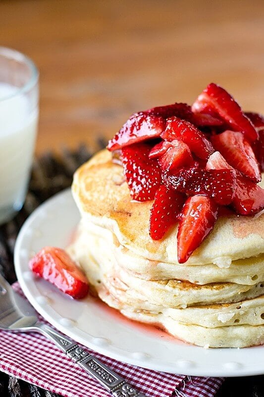 Strawberry Shortcake Pancakes by tastes of lizzy t stacked on a white plate with a silver fork  and red gingham napkin on the side.