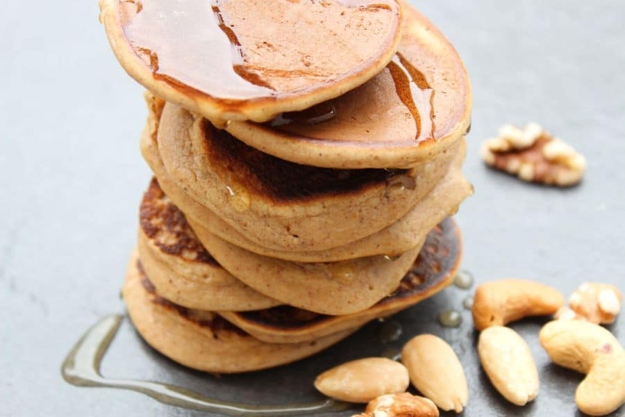 banana and nut pancakes by free from fairy stacked on a grey surface toppes with syrup and nuts