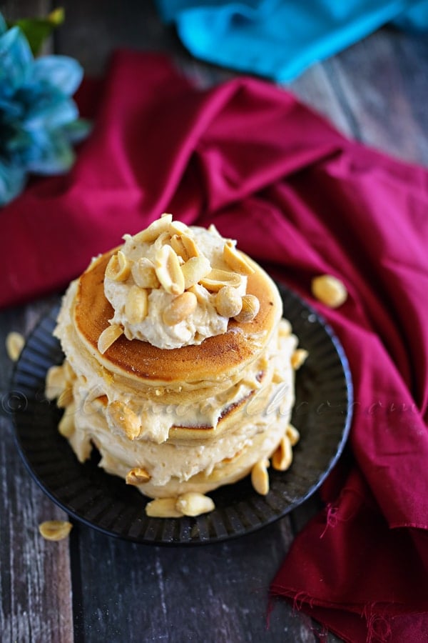 peanut butter overload pancakes by kleinworth & co stacked on a small black plate topped with cream and nuts.