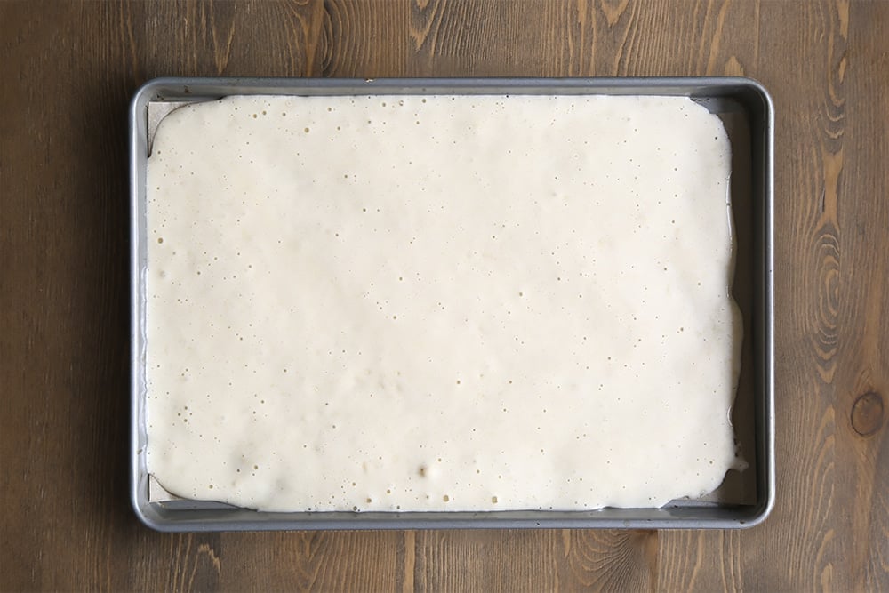 a baking tray lined with greaseproof paper with the vanilla cake batter poured in a thin layer.