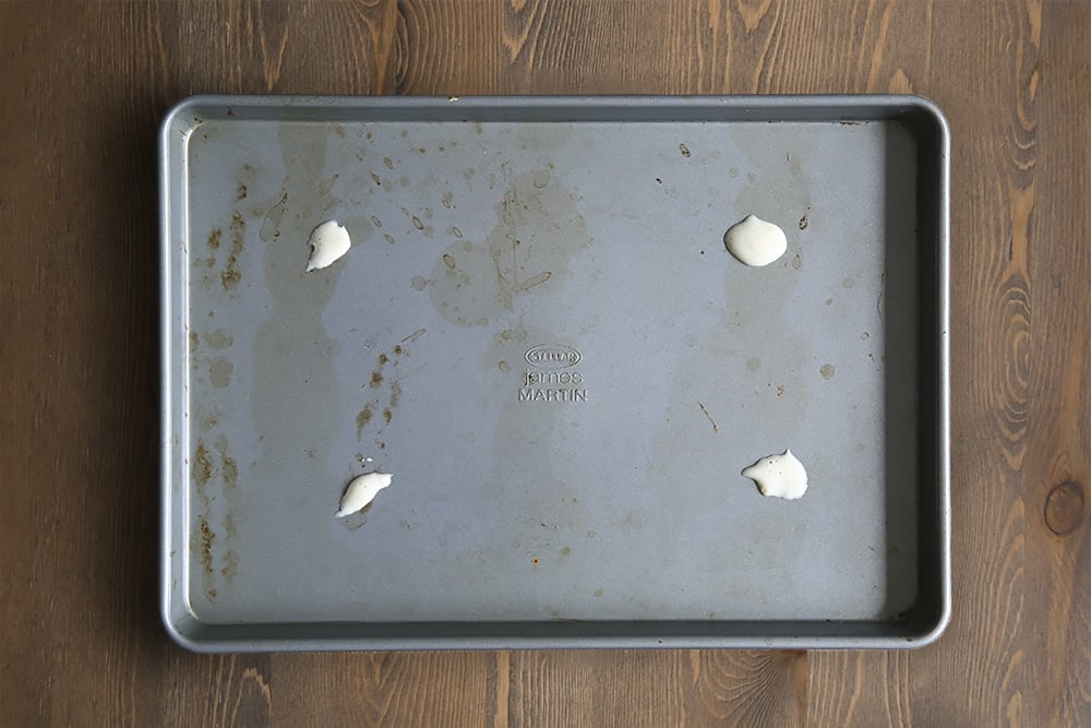 a baking tray on a wooden background with 4 blobs of cake batter on.